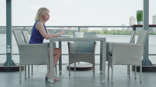 Bored Nervous Woman Sitting at the Table in Outdoor Cafe Waiting. Wide Shot Side View of Elegant alt