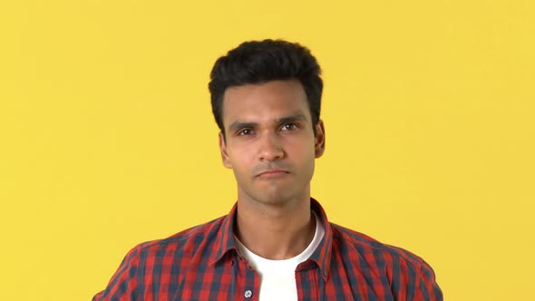 Young Indian man in plaid shirt saying yes by shaking his head against yellow background