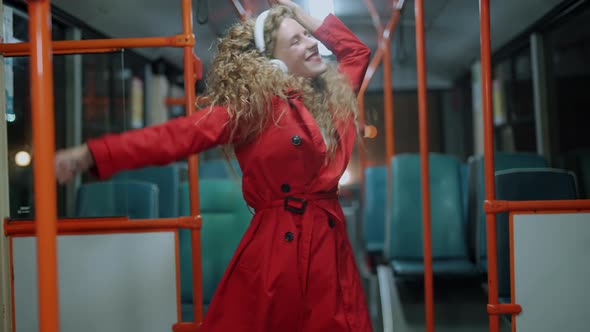 A Smiling Curly Woman in Headphones is Listening Music and Funny Dancing in Bus alt