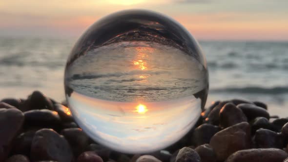 crystal ball lay on stones on the beach, ocean waves and sunset inside