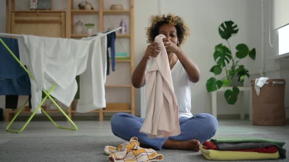 Black Housewife Woman Folding Clothes in Stack on in Living Room alt