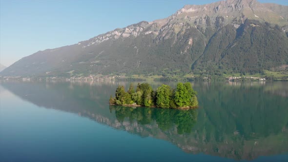 Droneshot of little island in Switzerland with mountain panorama in the back. Early morning light wi alt