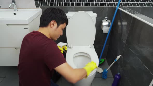 young man cleaning toilet bowl in bathroom