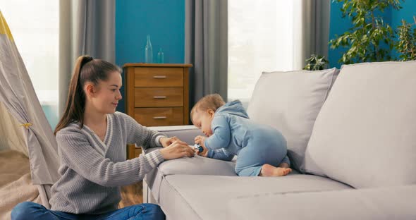 A Caring Mother is Sitting on Carpet in Cozy Living Room Watching Son Sitting on alt
