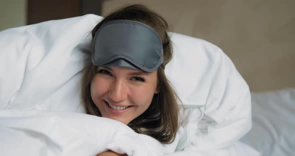 Emotional Lady with Sleep Mask and Soft Duvet Lies on Bed alt