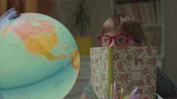 Curious Schoolboy Looking at Earth Globe From the Notebook alt