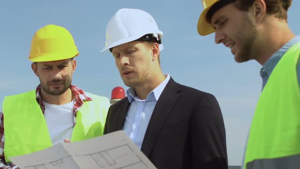 Male Architect in Suit and Safety Helmet Discussing House Scheme With Builders