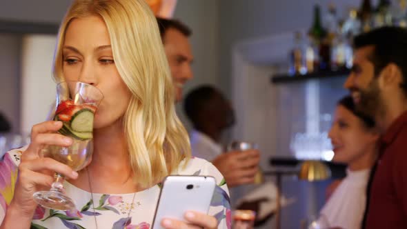 Beautiful woman using mobile phone while having cocktail alt