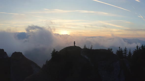 Person Standing on a Cliff Above the Clouds at Sunset 
