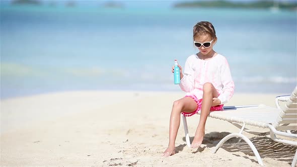 Little Adorable Girl with Bottle of Sun Cream Sitting at Tropical Beach