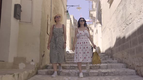 Two beautiful elegant young woman walking narrow streets of Matera