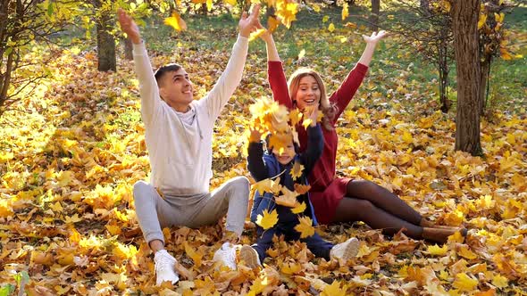 Lovely Family Throws Dry Yellow Leaves in Sunny Autumn Park alt