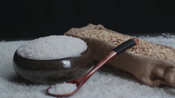 Raw Rice Grain In Unique Bowl, Rustic Bag And Wooden Spoon Rotate  alt