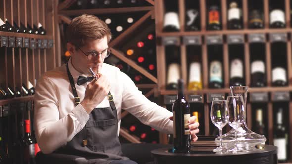 Elegant Young Sommelier with Bow Tie Uncorking Bottle of Wine in Wine Boutique. alt