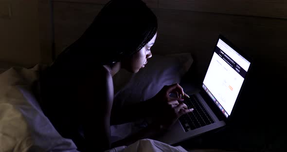Black Woman using laptop in bed at home.