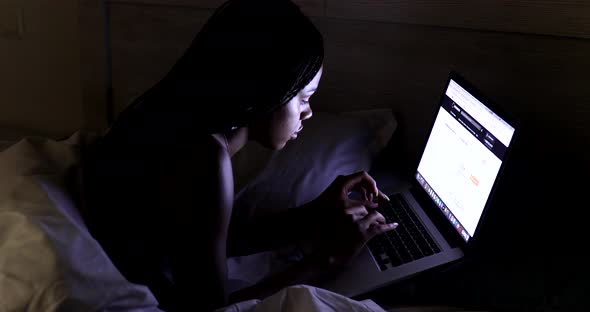 Black Woman using laptop in bed at home. alt