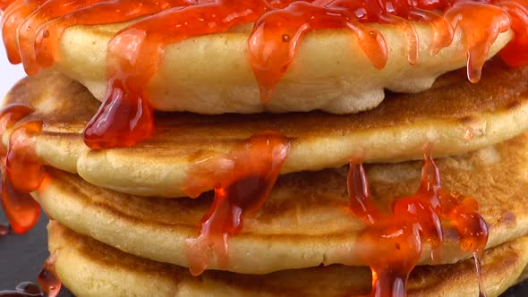 Pancakes with strawberry topping on a white background. Pancake lies on a black slate round stone. alt