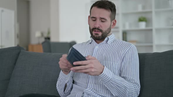 Worried Young Man Checking Empty Pocket for Money at Home  alt