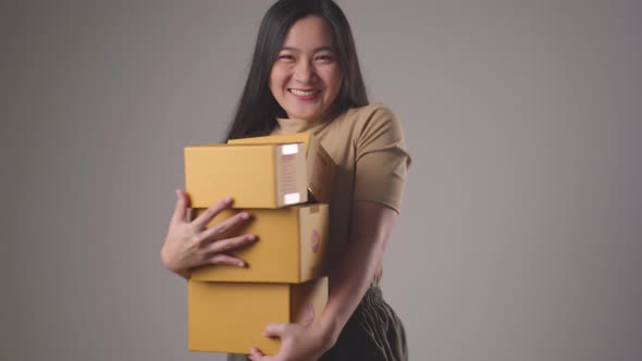 Confident asian woman happy holding stacks boxes dancing smilling and looking at camera