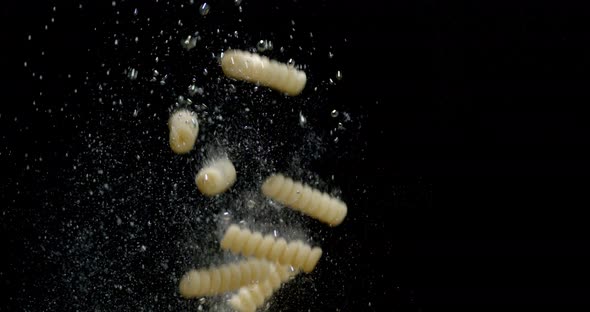 Fusilli Dry Pasta Falls Under Water with Air Bubbles.  alt