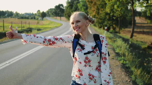 Traveler Woman Hitchhiking on a Sunny Road and Walking alt