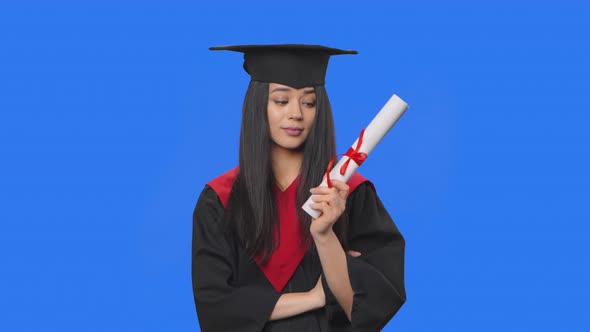 Portrait of Female Student in Graduation Costume Looking Thoughtfully at Her Diploma Then Rejoices alt