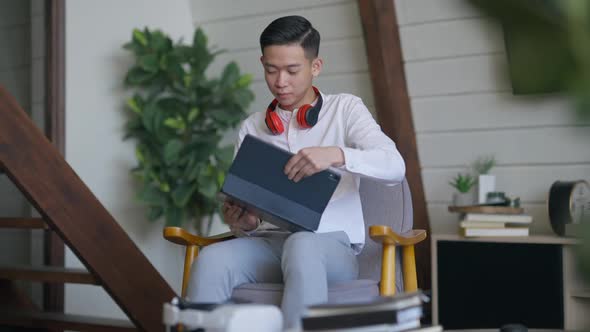 Young Asian Man Standing Up From Comfortable Armchair and Leaving Passing Camera alt