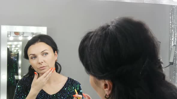 Young Beautiful Showy Woman in Front of a Mirror Applies Makeup and Foundation or Concealer with Her alt