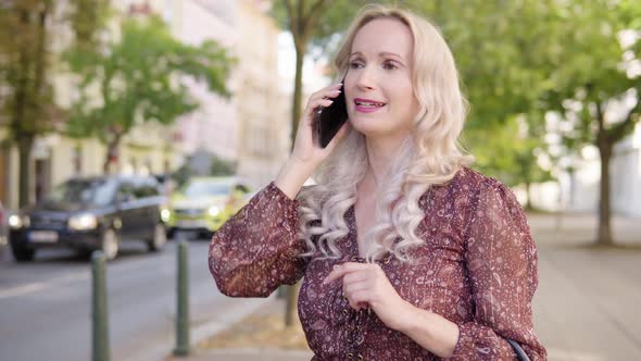 A Middleaged Caucasian Woman Talks on a Smartphone in an Urban Area  a City Street alt