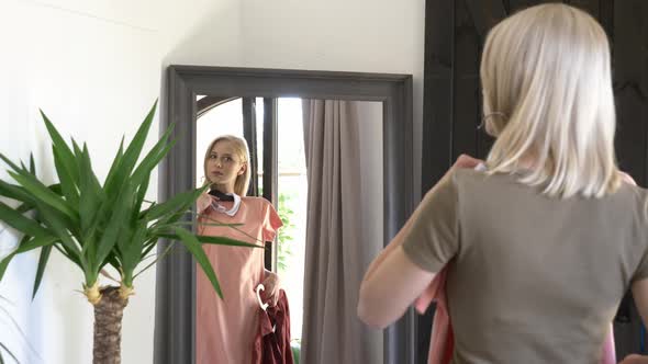 blonde girl chooses is dressing up a dress at mirror at home
