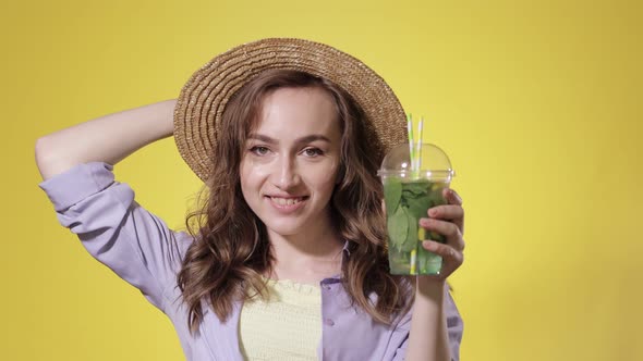 Surprised Woman Drink Mojito cocktail From Plastic Cup Over Yellow Studio Background alt