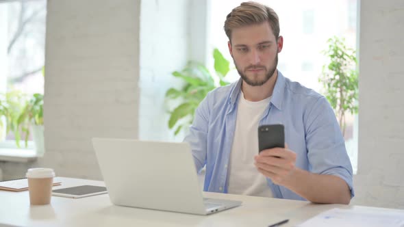 Creative Man with Laptop Using Smartphone in Modern Office alt