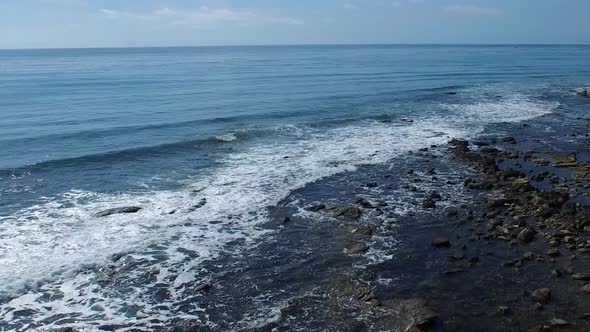 Tracking shot of a young man running on a rocky ocean beach shoreline. alt