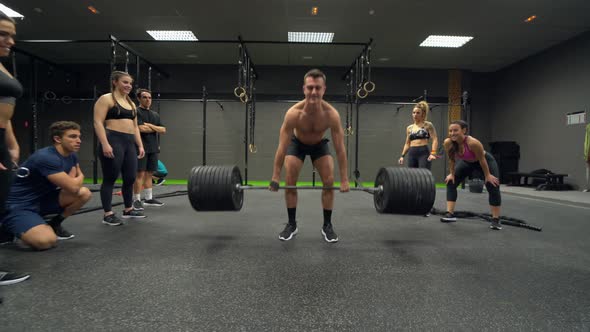 Athletes cheering man while lifting weight at gym