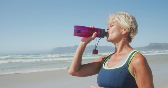 Athletic woman drinking water on the beach alt