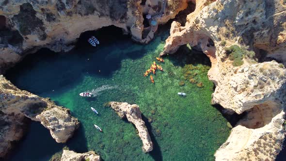 Drone shot of kayaks and boats passing in the ocean, people exploring caves and tunnels.