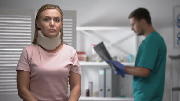 Sad Female in Foam Cervical Collar Looking at Cam, Doctor Examining X-Ray Result