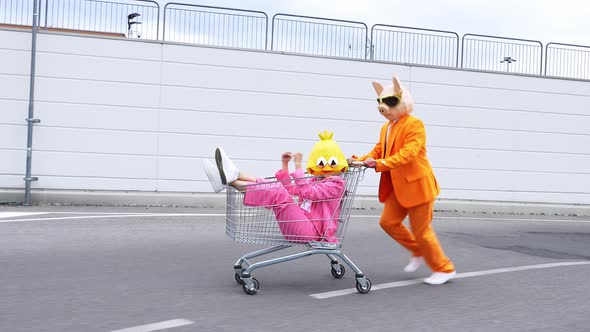 Man pushing woman shaking fist in shopping cart, wearing animal masks