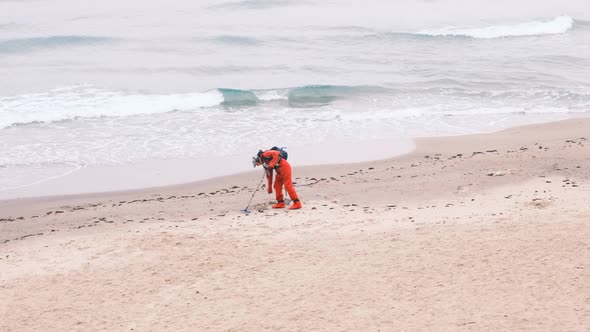 Man Walks with a Metal Detector in the Sand