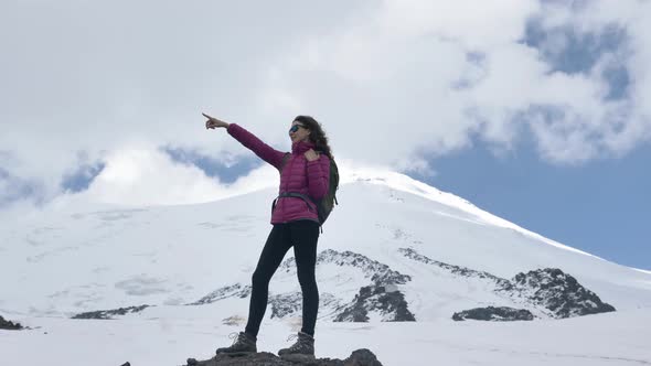 Female Climber in Sunglasses Points the Way with Her Finger Standing on a Stone Against the alt