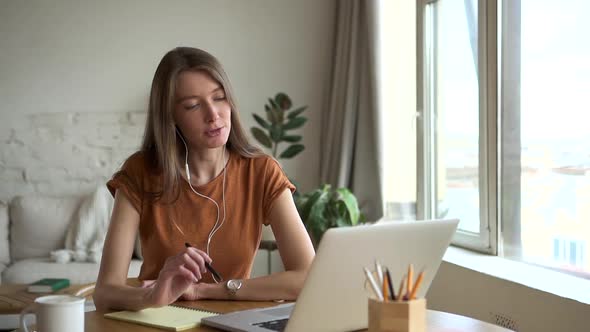 Young Woman Talking in Front of Laptop Screen During Online Education at Table at Home alt