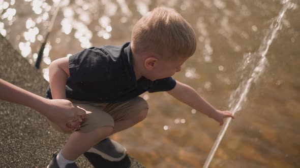 Joyful Child Touches Water Jet Holding Mother Hand on Square alt