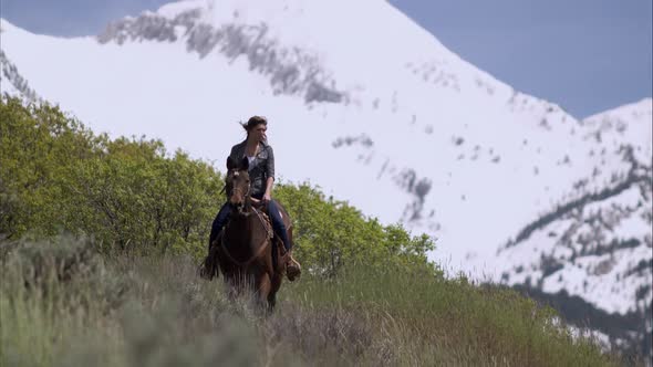 Slow motion shot of a woman on horseback galloping down a hill alt
