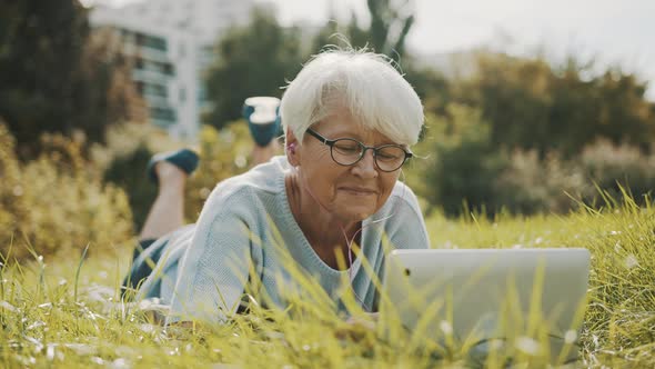 Senior Retired Woman Using Laptop in the Nature While Lying on the Grass alt