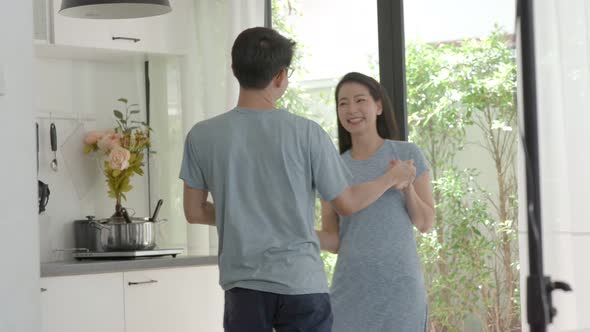 Asian Couple husband and wife having fun dancing together in house kitchen.