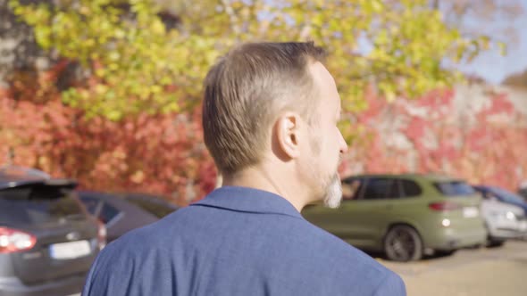 A Middleaged Caucasian Man Walks Across a Parking Lot in a Small Town in Fall  View From Behind