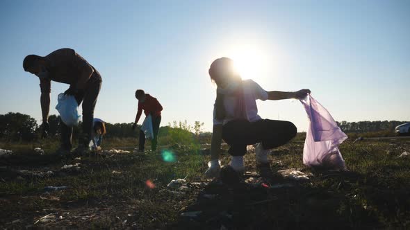 Young Parents with Two Kids Collecting Trash in Bags at Lawn Near Roadside alt