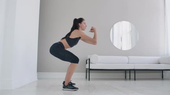 Slender Brunette Woman Performs a Series of Squats at Home in Slow Motion alt