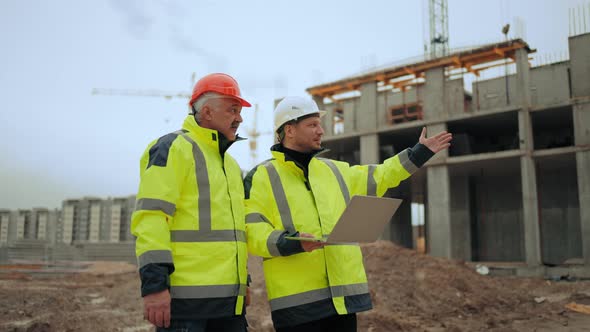 Two Foremen in Hard Hats and Uniform are Walking on Building Area of Modern Residential Complex alt