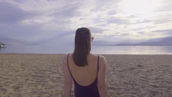 Rear view of attractive girl sitting on a sandy mountain beach alt